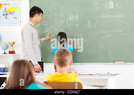 Scuola elementare studente iscritto risposta sulla scheda con insegnante in piedi accanto a lei Foto Stock