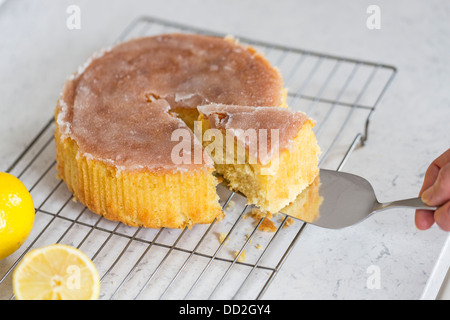 Home limone al forno cospargere la torta su una griglia di raffreddamento con glassa di zucchero superiore, una fetta sollevato su una fetta di torta e due limoni Foto Stock