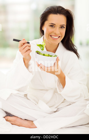 Elegante giovane donna in pigiama insalata mangiare sul letto Foto Stock