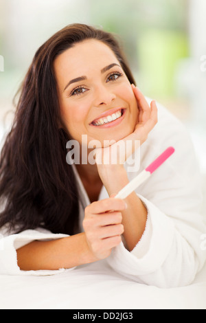 Donna felice giacente sul letto tenendo un test di gravidanza Foto Stock