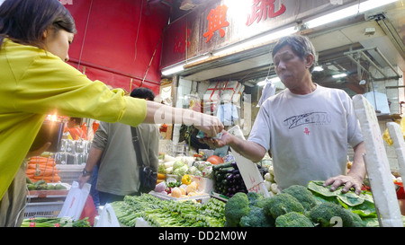Un cliente di consegnare il denaro a un titolare di stallo a Hong Kong mercato alimentare. Foto Stock