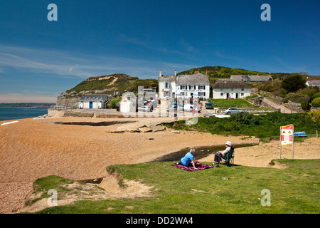 Una coppia di anziani in spiaggia Seatown guardando verso l'Anchor Inn e Golden Cap sul SW sentiero costiero. Il Dorset, England, Regno Unito Foto Stock