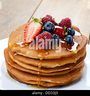 Piastra di colore bianco pieno di pancake con Fragole Lamponi Mirtilli e miele Foto Stock