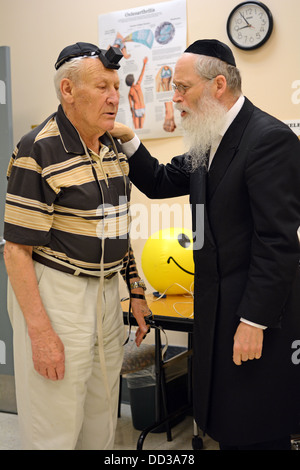 Un religioso rabbino ebreo in visita a un senior center nella spiaggia di Brighton Brooklyn incoraggiare gli immigrati russi per mettere su phylacteries Foto Stock