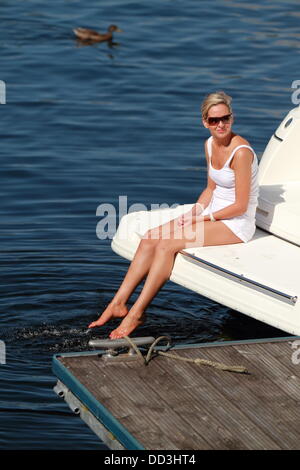 Una bella donna siede sulla estremità di una barca con i suoi piedi in acqua, Luss, Loch Lomond Scozia, Regno Unito Foto Stock