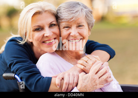 Allegra donna di mezza età che abbraccia disabili madre senior all'aperto Foto Stock