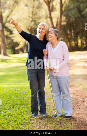 Amare di mezza età figlia prendere senior madre per una passeggiata all'aperto nella foresta Foto Stock