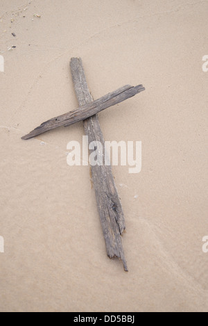 Una croce fatta di driftwood recante su di sabbia su una spiaggia. Foto Stock