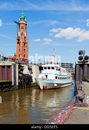 Imbarcazione turistica passando Neuer Hafen nave bloccare a Bremerhaven, Simon-Löschen-Turm faro in background Foto Stock