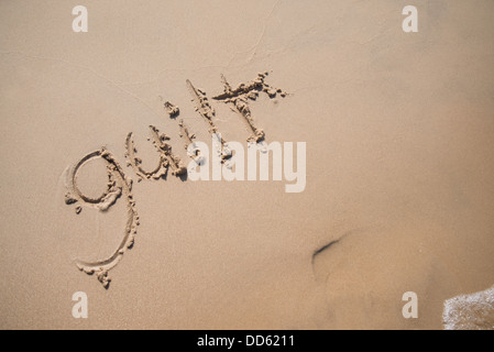 La parola "colpa" scritto nella sabbia, essere lavato via da un'onda. Foto Stock