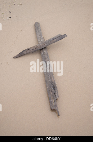 Una croce fatta di driftwood recante su di sabbia su una spiaggia. Foto Stock