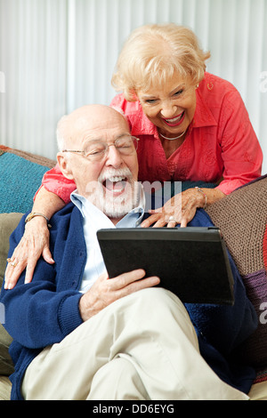 Coppia senior divertirsi e ridere mentre usando il loro tablet pc. Foto Stock