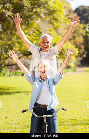 Felice giocoso coppia senior avendo divertimento bicicletta equitazione all'aperto Foto Stock