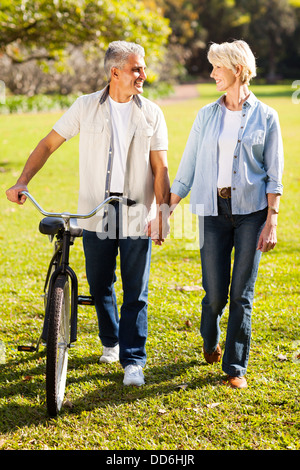 Bella coppia senior a piedi una bici nel Parco tenendo le mani Foto Stock