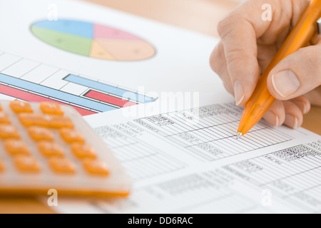 Mano con penna arancione e calcolatrice verifica dati del foglio di calcolo Foto Stock