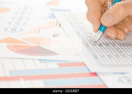 Mano con penna blu lavorando su fogli di calcolo e grafici Foto Stock