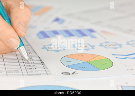 Mano con penna lavorando su fogli di calcolo e grafici Foto Stock