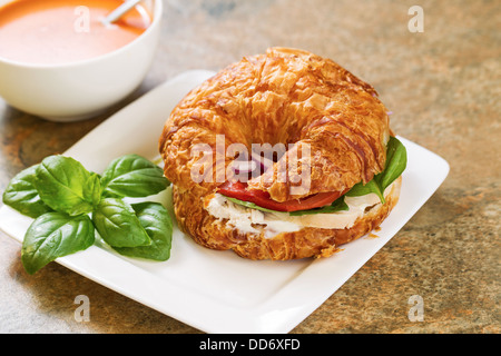 La foto in orizzontale di un'insalata di pollo, pomodoro, il basilico e la cipolla all'interno di croissant pane bianco sulla piastra quadrata con zuppa di pomodoro Foto Stock