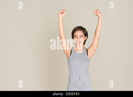 Giovane donna sorriso e festeggiare il successo con le braccia sollevate Foto Stock