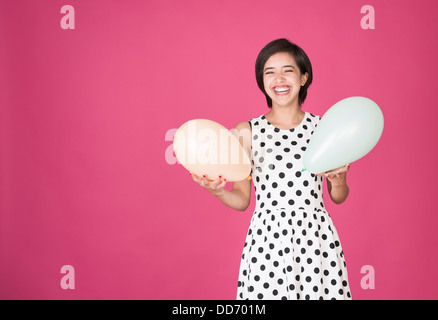 Giovane e bella donna multirazziale divertendosi con due palloncini a celebrazione Foto Stock