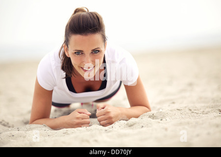 Sorridente donna fitness all'aperto facendo esercizio sulla spiaggia Foto Stock