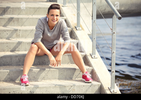 Stanco giovane atleta donna seduta sulle scale avente la sua rottura Foto Stock