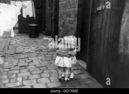 Due giovani ragazze abbraccio in lastricato della strada sul retro della casa a schiera a Oldham, Lancashire. Foto Stock