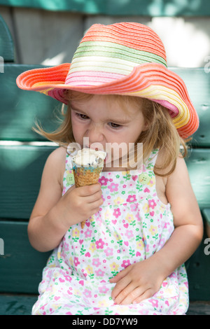 La ragazza bionda indossa un abito floreale, colorato hat e mangiare un gelato. Foto Stock