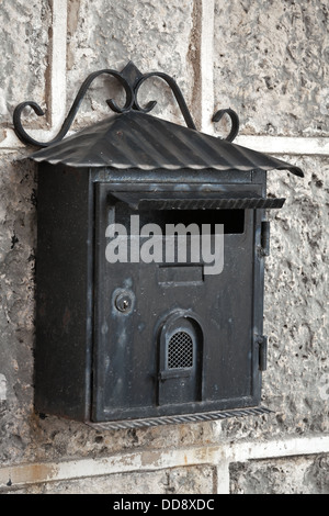 Vecchio weathered nero mailbox di metallo montata su grigio muro di pietra Foto Stock