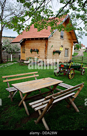 Antiche in legno log cabin, tavolo con panche e un vecchio vagone tirato da cavalli nel cortile agriturismo. Foto Stock