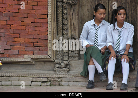 Studentesse in uniforme in seduta Durbar Square, Patan. Foto Stock