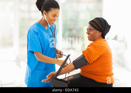 Sorridente infermiera africana senior di controllo pressione del sangue del paziente Foto Stock