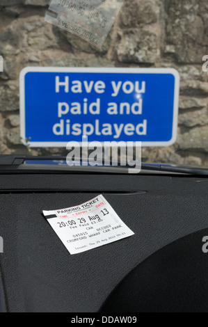 Pagare e visualizzare i biglietti per il parcheggio visualizzata sul cruscotto di un'automobile con avete pagato e segno visualizzato in background England Regno Unito Foto Stock