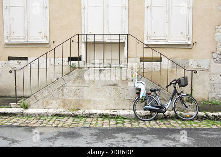 Bicicletta con seggiolino per bambini, appoggiata contro le vecchie scale di pietra Foto Stock