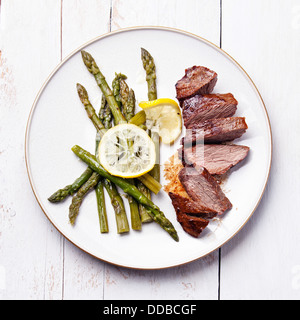 Arrosto di manzo con asparagi bianchi su sfondo di legno Foto Stock