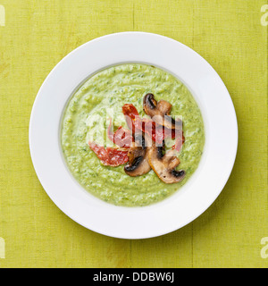 Verde zuppa di piselli in ciotola sul bianco sullo sfondo di legno Foto Stock