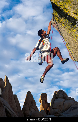 Scalatore di lotte per il vertice di un impegnativo pinnacle come nuvole temporalesche costruire dietro di lui. Foto Stock