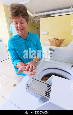 Senior donna contando il cambiamento per una lavatrice commerciale in una sala lavanderia Foto Stock