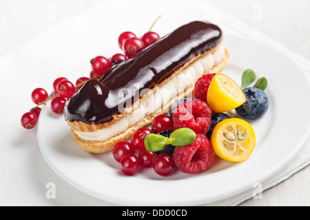 Eclair al cioccolato con frutti di bosco sulla piastra bianca Foto Stock