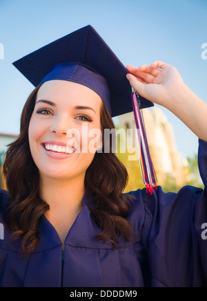 Felice la laurea razza mista donna nel cappuccio e camice celebrando in campus. Foto Stock