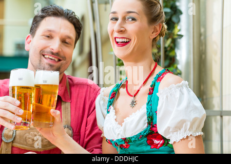 Coppia giovane in tradizionali bavaresi Tracht nel ristorante o pub con birra Foto Stock