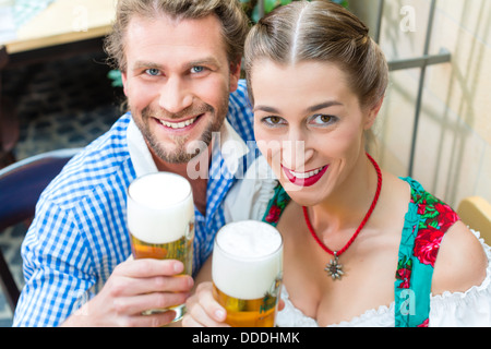 Coppia giovane in tradizionali bavaresi Tracht nel ristorante o pub con birra Foto Stock