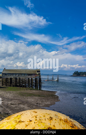 Una vista del Lubec, Maine seashore con un grande giallo del galleggiante in metallo in primo piano e un vecchio impianto di pesce in background. Foto Stock