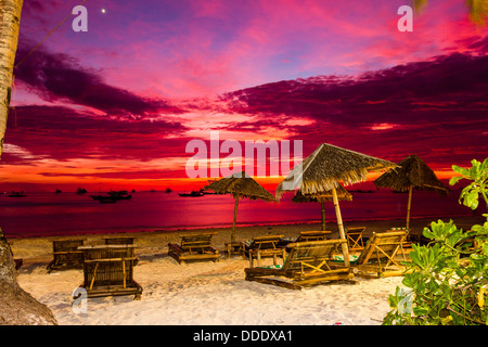 Viola e arancione nel cielo come il sole tramonta su una spiaggia tropicale Foto Stock