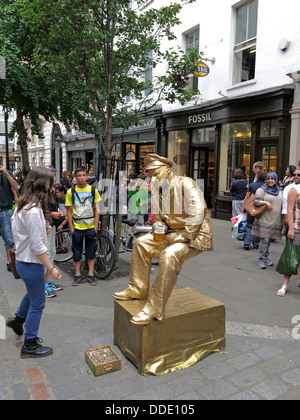 Street performer busker vestito d'oro seduto su una sedia invisibile in Covent Garden, Londra Foto Stock