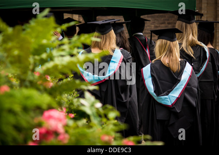 Linea di laureati fino a inserire la loro cerimonia. Essi sono tutti rivolta lontano dalla telecamera con i loro abiti cerimoniali mostra. Foto Stock