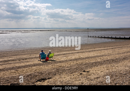 Coppia di anziani seduto da solo su una spiaggia deserta. Sole estivo. Foto Stock