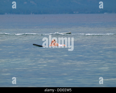 Stanco surfista femmina in mare sulla parte superiore della tavola da surf con le mani in faccia Foto Stock