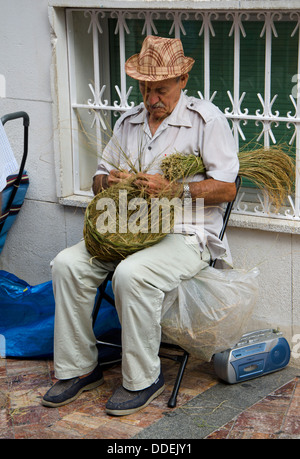 Uomo spagnolo tessitura di un paniere di erba spagnolo nelle strade di Nerja, Andalusia, Spagna. Foto Stock