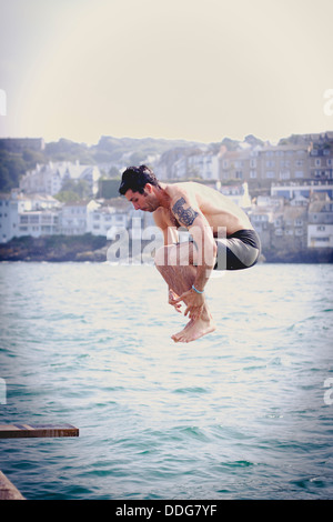 Un uomo che si tuffano da un fatto in casa scheda diving in banchina a St. Ives, Cornwall Foto Stock